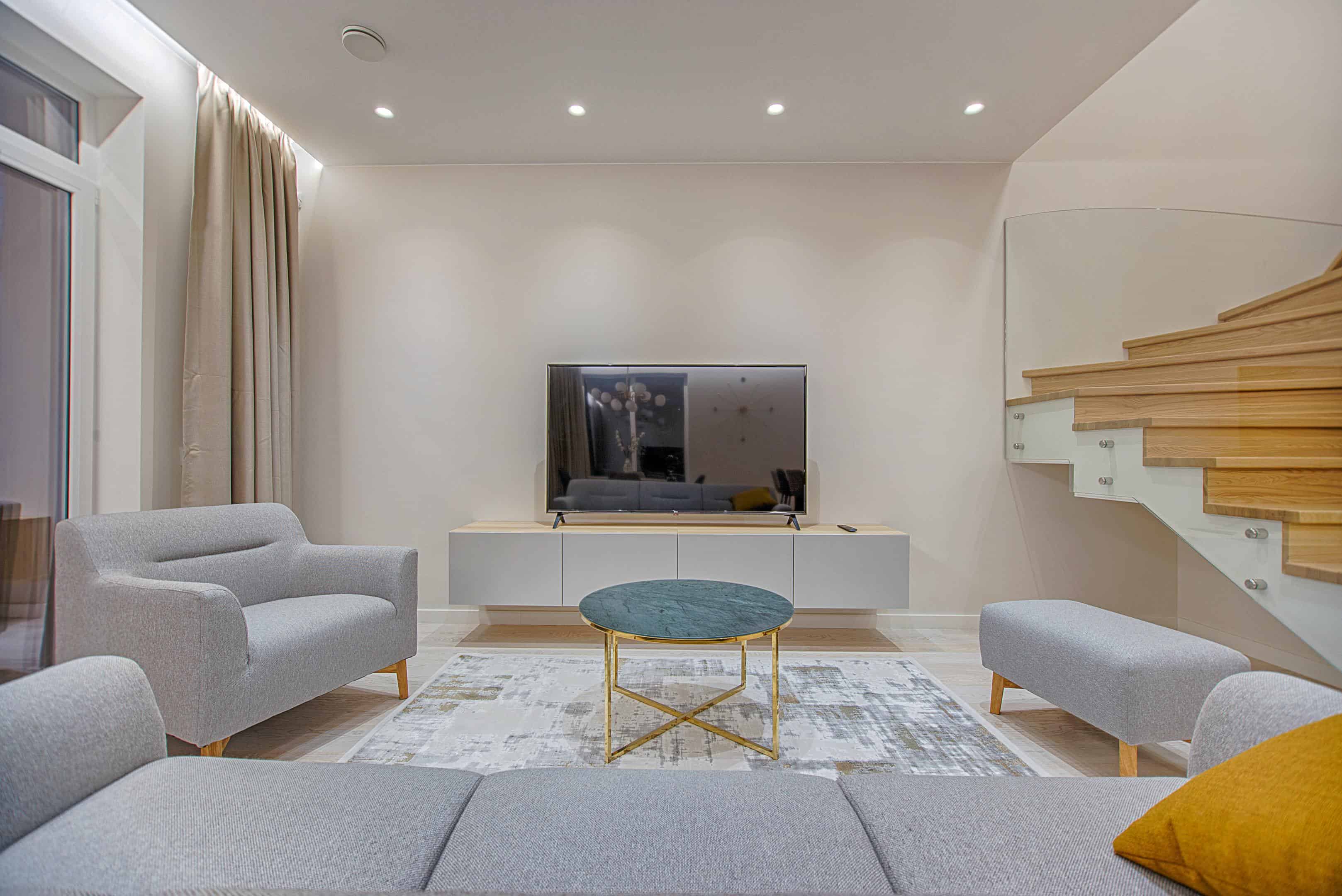 Living room lit by downlights with a large wall-mounted television