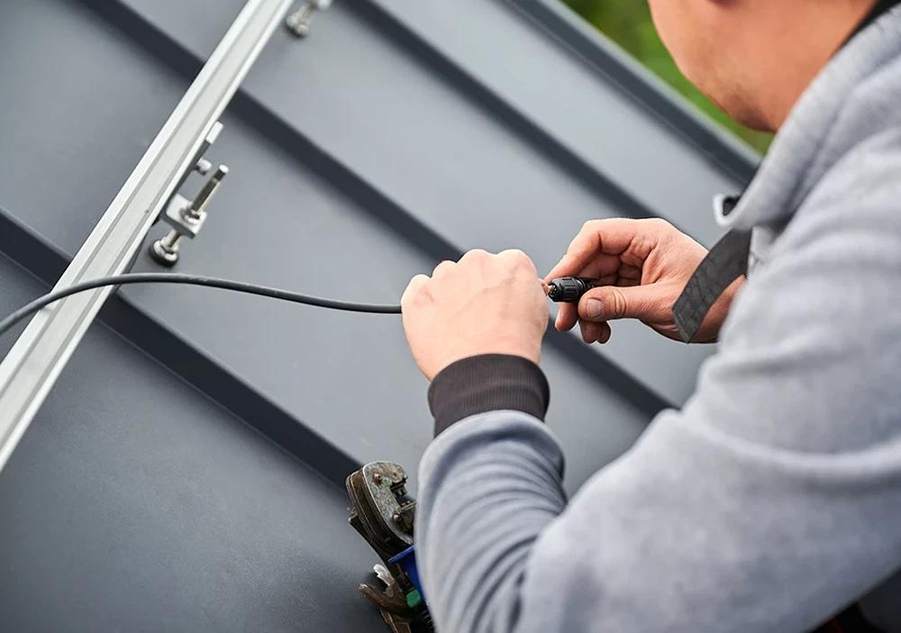 A technician working on solar panel cabling at roof level